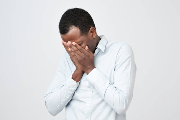 istock Adult african man with sad expression covering face with hands while crying. 1062101080