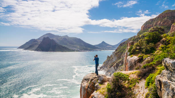 Man standing on cliff edge photographing sea and landscape