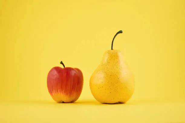 Yellow pear and red apple on a yellow background. Fruit home decor. Plastic decorative fruit