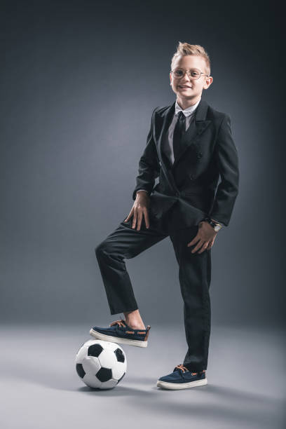 istock boy dressed as businessman with soccer ball looking at camera on grey background 1062125216