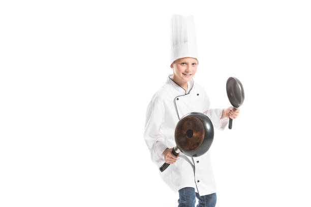 istock smiling boy in white chef uniform and hat holding frying pans isolated on white 1062127286