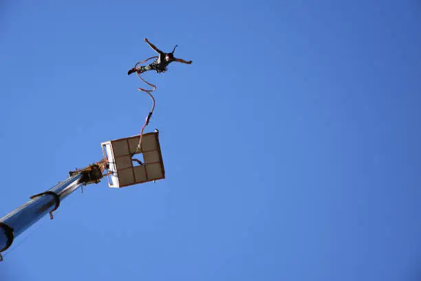 Bungee jumping from a 50-metre-high crane during Sofia Extreme Sports Festival. Seen from the ground man falling down from a platform high in the blue sky