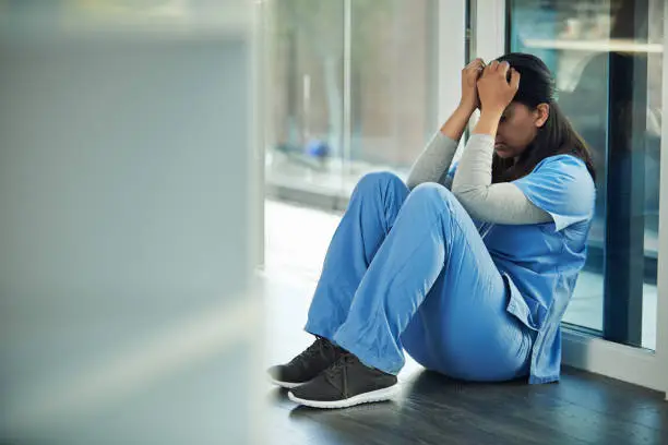 Shot of a young doctor sitting on the floor and looking distraught