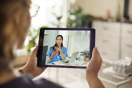 Over the shoulder shot of a patient talking to a doctor using of a digital tablet