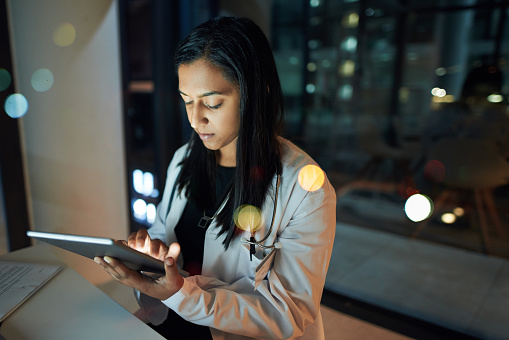 Shot of a young doctor using a digital tablet in an office at night
