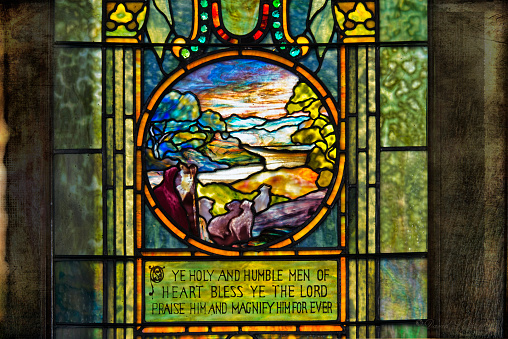 Stained Glass Church Window with the words, “Ye holy and humble men of heart, bless ye the Lord praise Him and magnify Him for ever”.