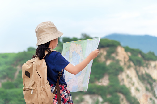 Children asian girl holding maps and  Magnetic compass travel backpacks standing in the mountain for education nature. Travel Concept