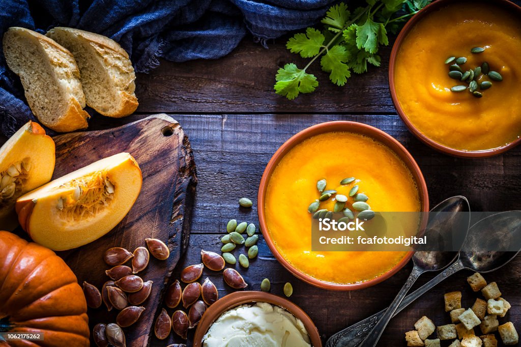 Pumpkin soup with ingredients on rustic wooden table Two brown bowls filled with homemade pumpkin soup surrounded by ingredients for preparing soup shot from above on rustic wooden table. Predominant colors are orange and brown. Low key DSRL studio photo taken with Canon EOS 5D Mk II and Canon EF 100mm f/2.8L Macro IS USM. Autumn Stock Photo
