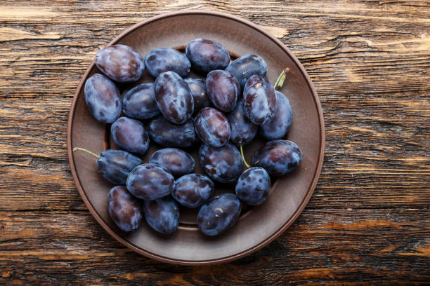 istock plums in a clay plate on a shabby wooden table. 1062204098