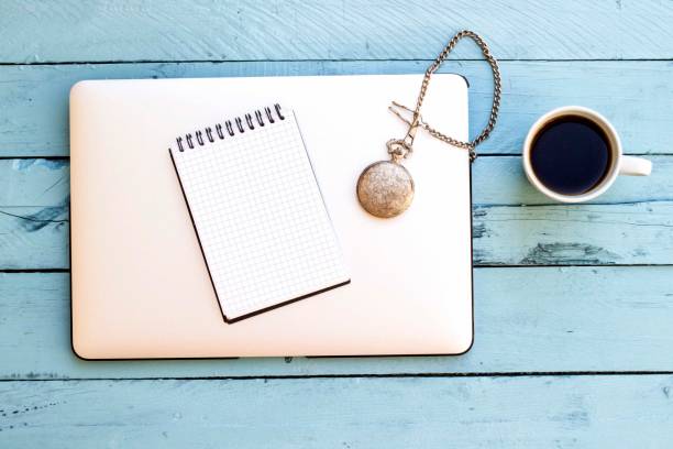notebook, old watch and laptop on blue wooden table