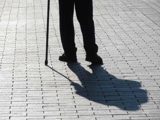 istock Silhouette of old man walking with a cane, long shadow on pavement 1062225904