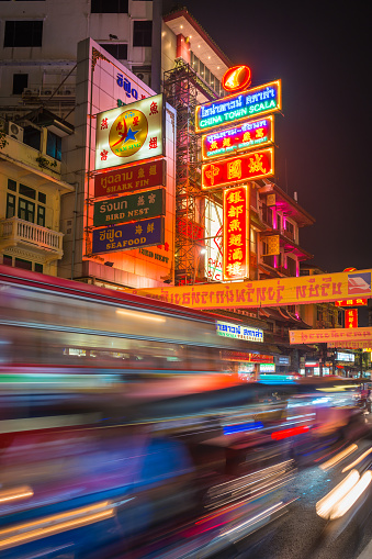 Colourful neon signs glowing in the night sky above the zooming traffic of Yaorawat Road in the Chinatown district of Bangkok, Thailand’s vibrant capital city.