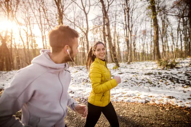 Photo of Couple running side by side in woods in winter.