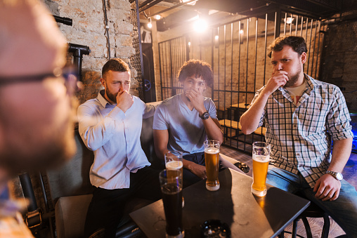 Man smoking in pub and his friends coughing. Anti smoking concept.