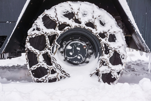 Closeup of a snowy chained wheel of a snow plow in winter