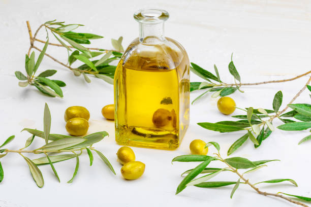 istock Extra virgin olive oil in glass bottle. Foreground. Includes leaves and olive branches. On white textured background. 1062259496