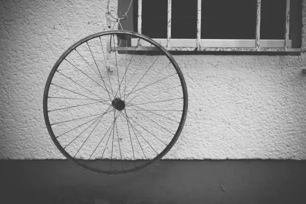 Bicycle wheel without a tyre hanging outside the window on the white wall of the house, viewed in close-up