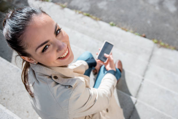istock Young woman using a smart phone outdoors and looking at camera 1062283092