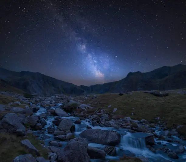 Stunning vibrant Milky Way composite image over Landscape image of river flowing down mountain range near Llyn Ogwen and Llyn Idwal in Snowdonia
