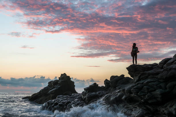 멕시코에서 극적인 일몰 동안 해변에 서 있는 여자 - beauty in nature cloud rocky coastline rock 뉴스 사진 이미지