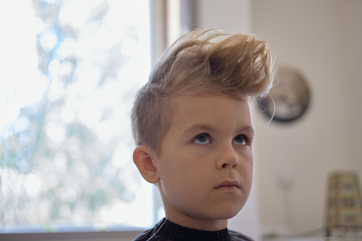 Cute little boy with hairstyle, sitting at home. Weird haircut made by mom