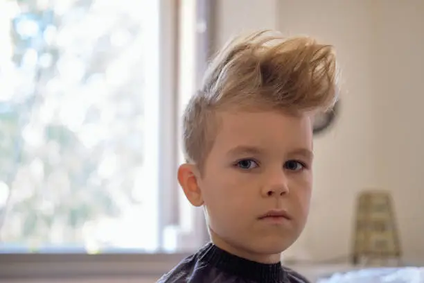 Cute little boy with hairstyle, sitting at home. Weird haircut made by mom