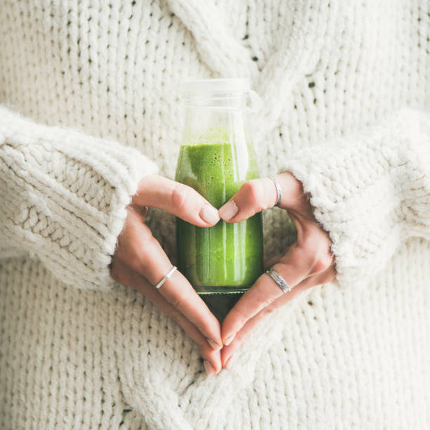 Winter seasonal smoothie drink detox in woman's hands, square crop Winter seasonal smoothie drink detox. Female in sweater holding bottle of green smoothie or juice making heart shape with her hands, square crop. Clean eating, weight loss, healthy dieting food concept detox stock pictures, royalty-free photos & images