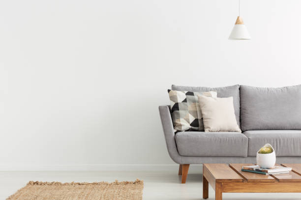 istock Wooden table in front of grey sofa with cushions in white flat interior with copy space. Real photo 1062314866