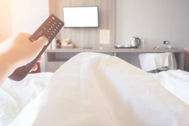 hand holding remote control television ob bed in bedroom close up stock photo