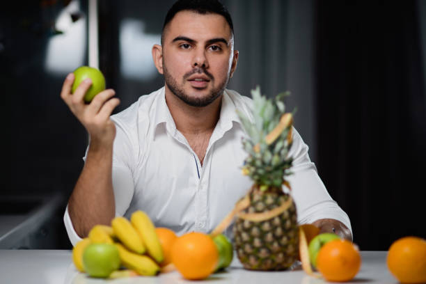 istock Attractive man with an apple in his hand sitting at a table on which lie fresh fruit. The concept of a healthy lifestyle 1062402582