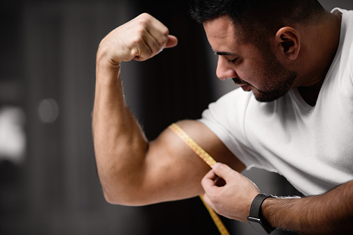 Athletic man measures his bicep with a measuring tape. The concept of fitness and health