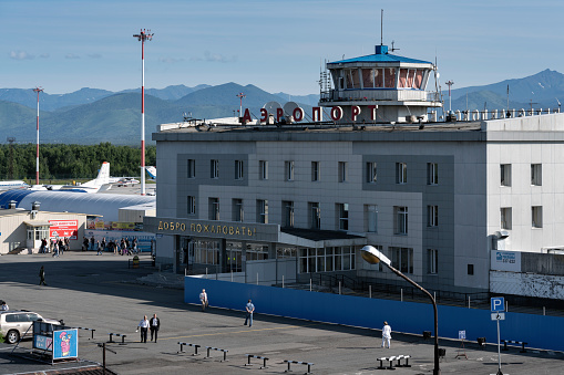 KAMCHATKA PENINSULA, RUSSIAN FAR EAST - AUGUST 6, 2018: Summer top view of building commercial airport terminal Petropavlovsk-Kamchatsky City (Yelizovo airport), passengers walking on station square.