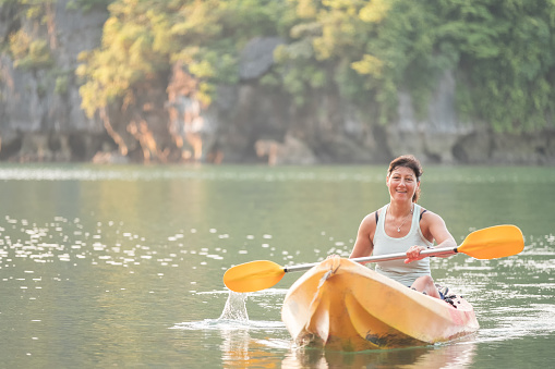 Morning kayaking - Eurasian woman paddling in front of remote Nam Cat Island, near Ha Long Bay, Vietnam