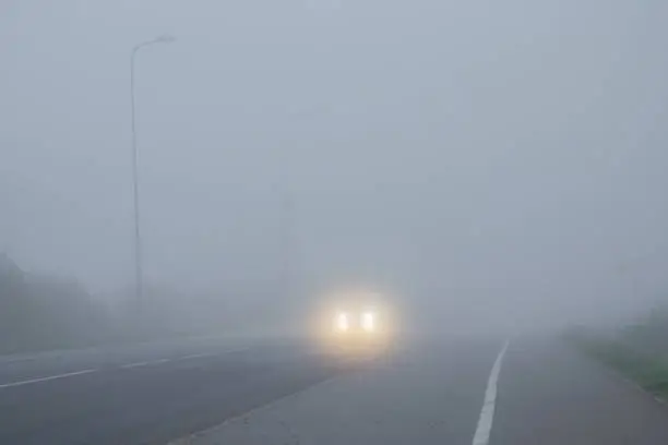 Photo of Poor visibility in fog on road. Car slowly driving in dangerous weather. Dark time. Traffic concept.