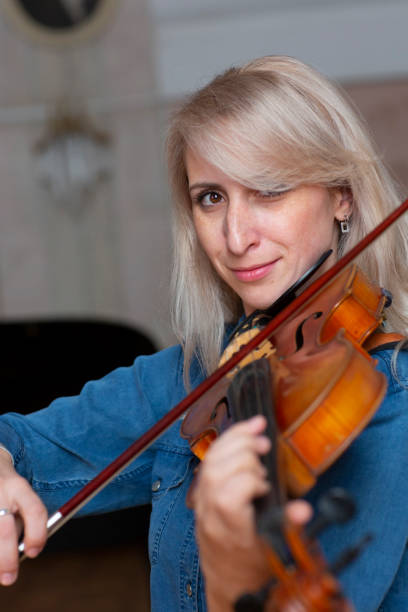istock Young beautiful woman with wavy blonde hair playing viola, holding bow hovering over instrument on her shoulder and smiling, looking at camera 1062425266