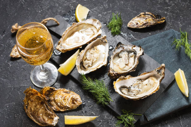 Opened Oysters and glass of white wine on dark texture background Opened Oysters and glass of white wine on dark stone texture background oyster stock pictures, royalty-free photos & images