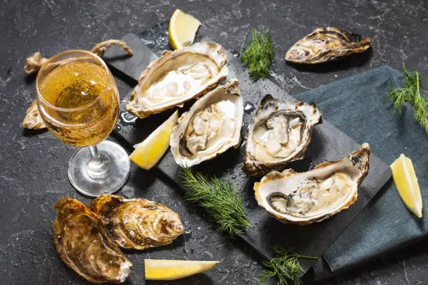 Photo of Opened Oysters and glass of white wine on dark texture background