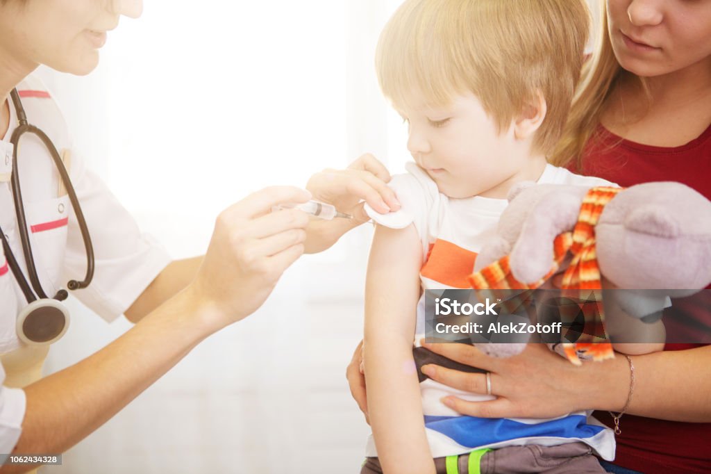 A doctor giving a child an injection at home A doctor giving a child an injection at home. Vaccination Stock Photo