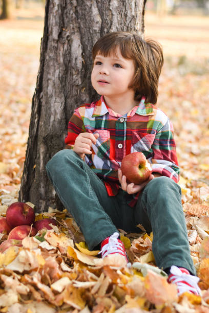 A boy lies on an autumn yellow leaf and eats an apple.