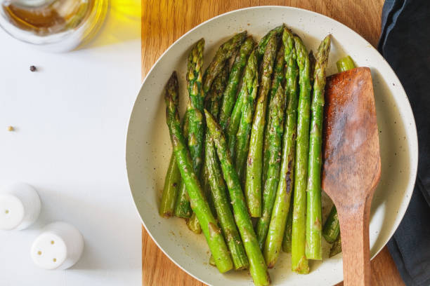 istock Top view on roasted asparagus in a white pan on a kitchen table. Modern style, vegetarian food. 1062453258