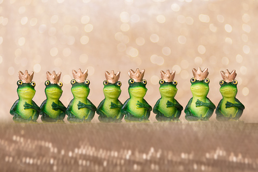 eight green frog princes standing in a row, hands on heart, flitter background