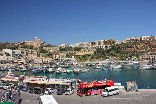 Gozo Ferry Terminal view Mgarr with touristic bus, snack bars, yachts and church on background Mgarr, Malta - May 2018: Gozo Ferry Terminal bay view of port with touristic bus, cars, snack bars, yachts and church on background mgarr malta island gozo cityscape with harbor stock pictures, royalty-free photos & images
