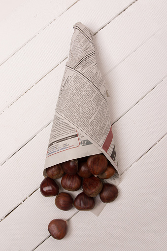 sweet chestnuts wrapped in newspaper on a white wooden background.