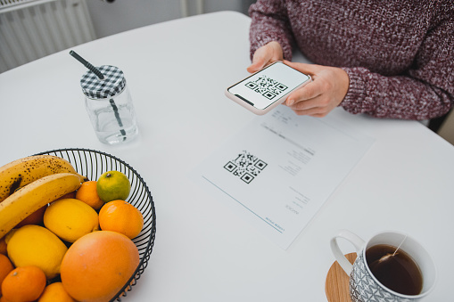 Woman scanning the qr code on a bill with a smart phone in the kitchen