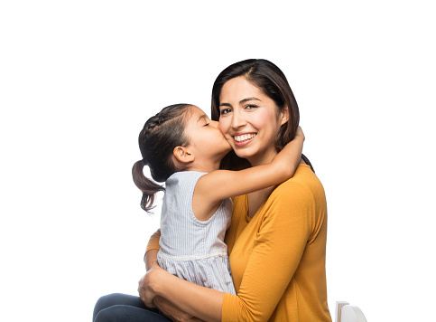 A beautiful little girl kissing her mother on the cheek while her mother smiles on an isolated white background
