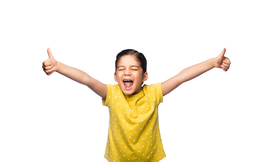 An excited little girl holding arms open with two thumbs up and yelling happily against an isolated white background