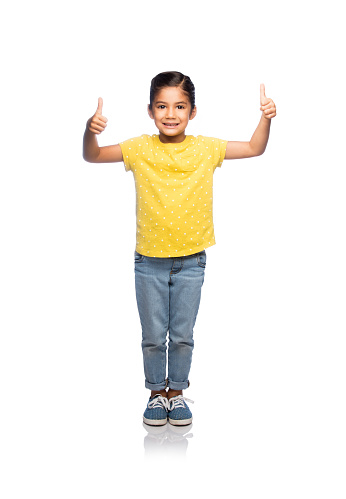 A very young little girl standing and giving two thumbs up against an isolated white background
