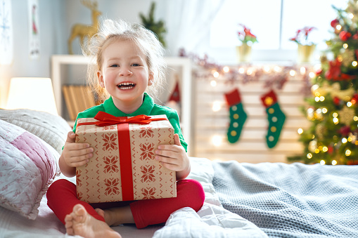 Happy holidays! Cute little child opening present near Christmas tree. The girl laughing and enjoying the gift.