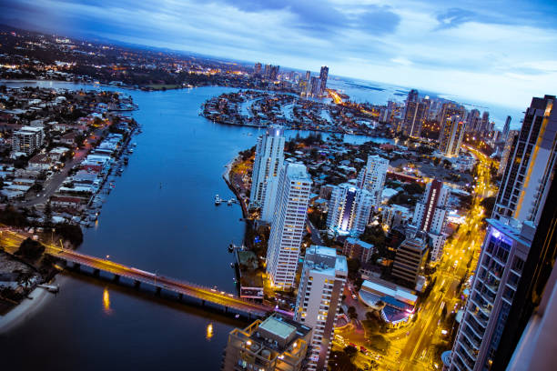Aerial view to modern Brisbane and Gold Coast Aerial photo of Brisbane with tall modern buildings and illuminated by yellow roads with vehicles and river with boats on cloudy sky background brisbane photos stock pictures, royalty-free photos & images