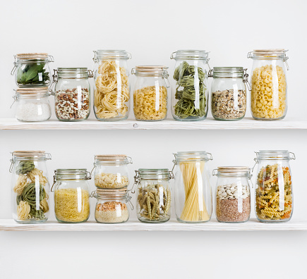 Various uncooked groceries in glass jars arranged on wooden shelves